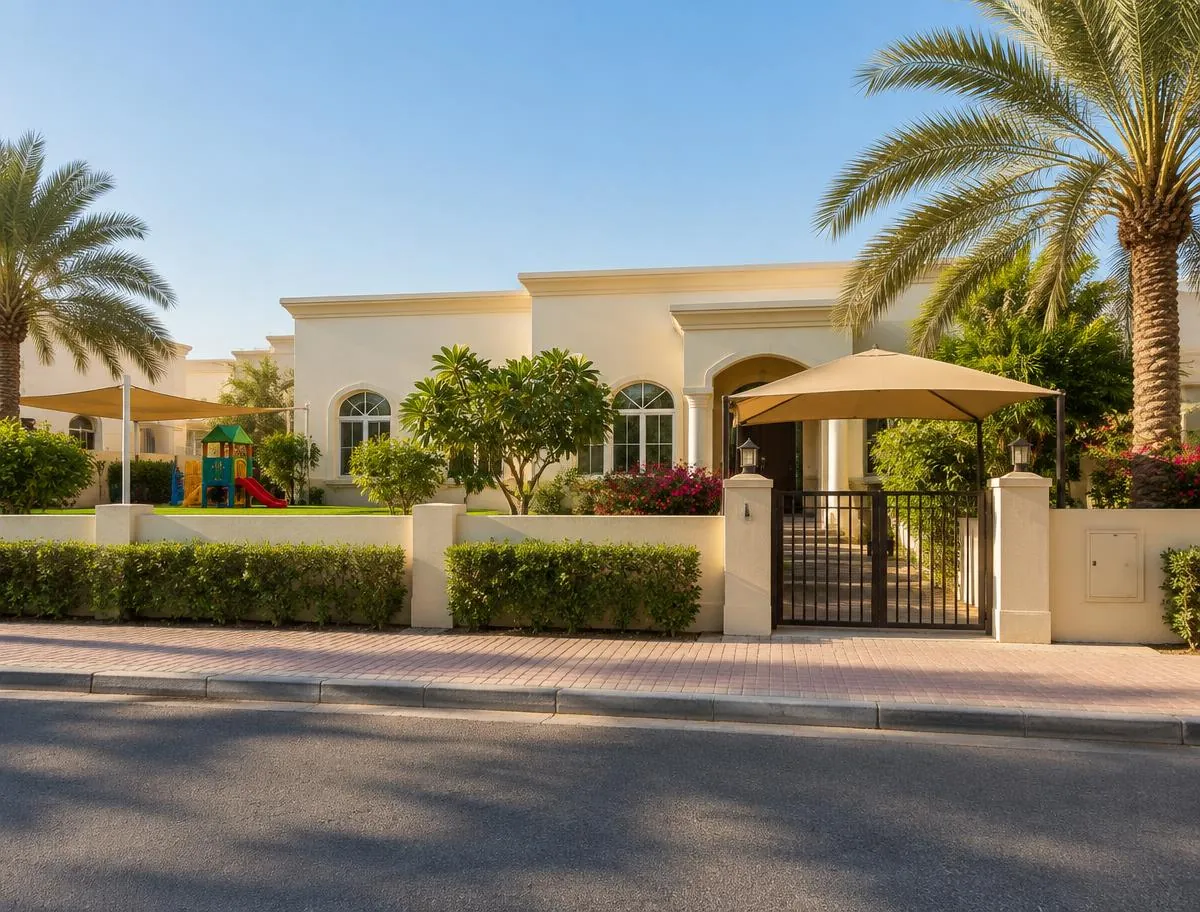 Cream villa-style building with palm trees and a shaded gate, seen from the street